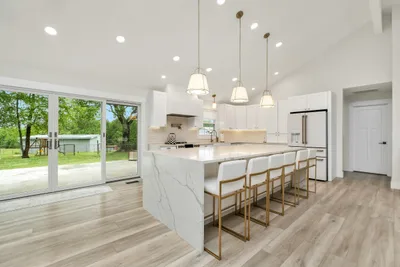 Remodeled kitchen with white cabinets, a stone waterfall island and a light wood floor